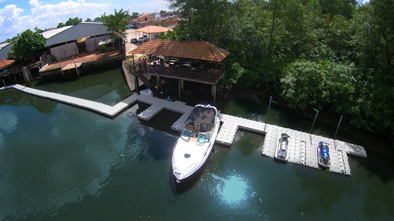 Vista aérea de píer flutuante modular Pierplas® da NTC Float com vagas secas para lancha e Jet Skis em propriedade à beira de um rio.