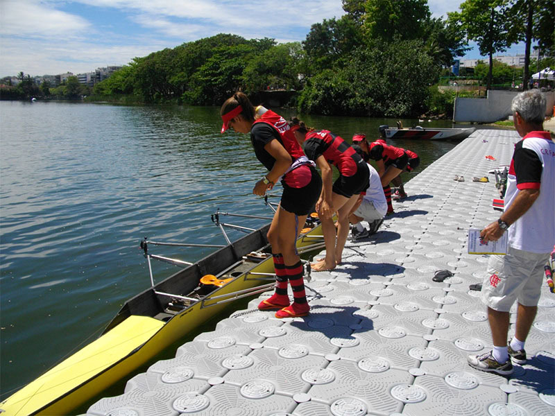Equipe de remo se preparando em uma plataforma flutuante modular antes de entrar no barco, às margens de uma lagoa.