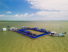 Vista aérea da piscina flutuante do evento AquaRace 2025, instalada sobre uma plataforma modular Pierplas no mar de João Pessoa (PB). A estrutura retangular, cercada por áreas azuis e repleta de espectadores, abriga atletas e equipes durante as provas de natação, com barcos de apoio ao redor.